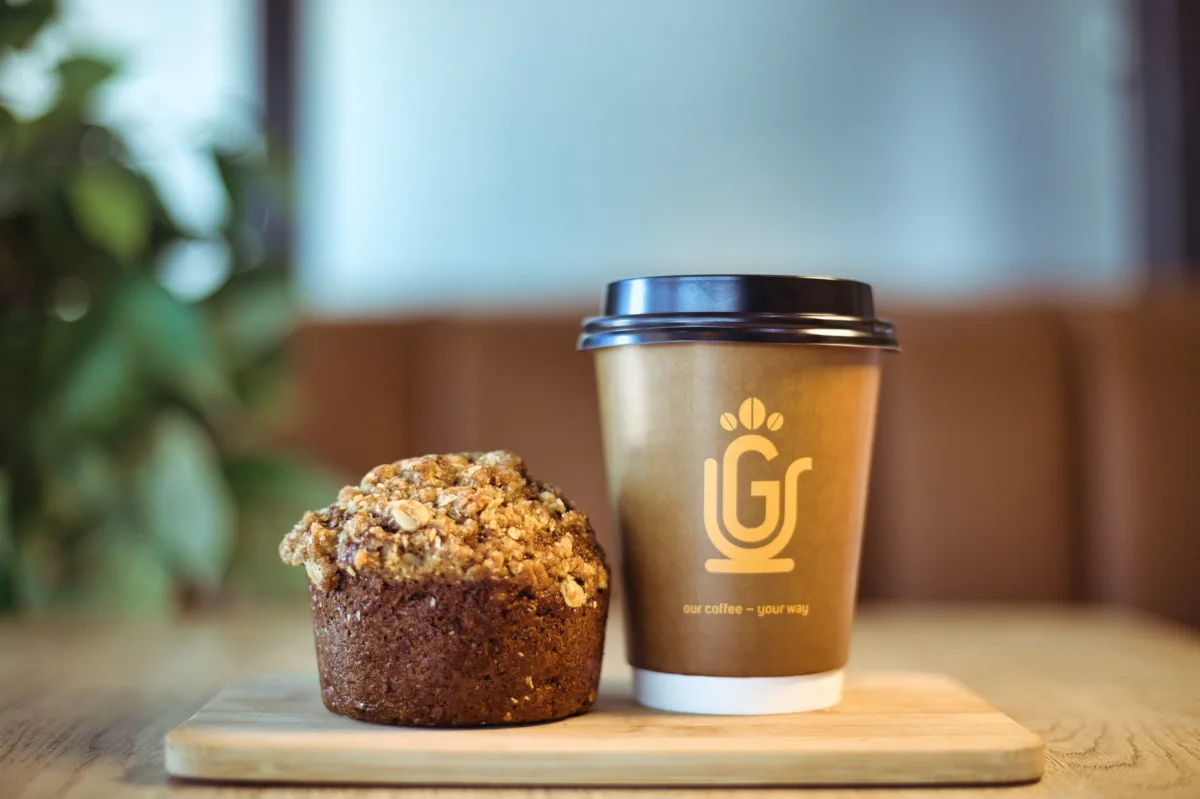 A Grande Cafe branded takeaway cup beside a crumb-topped muffin